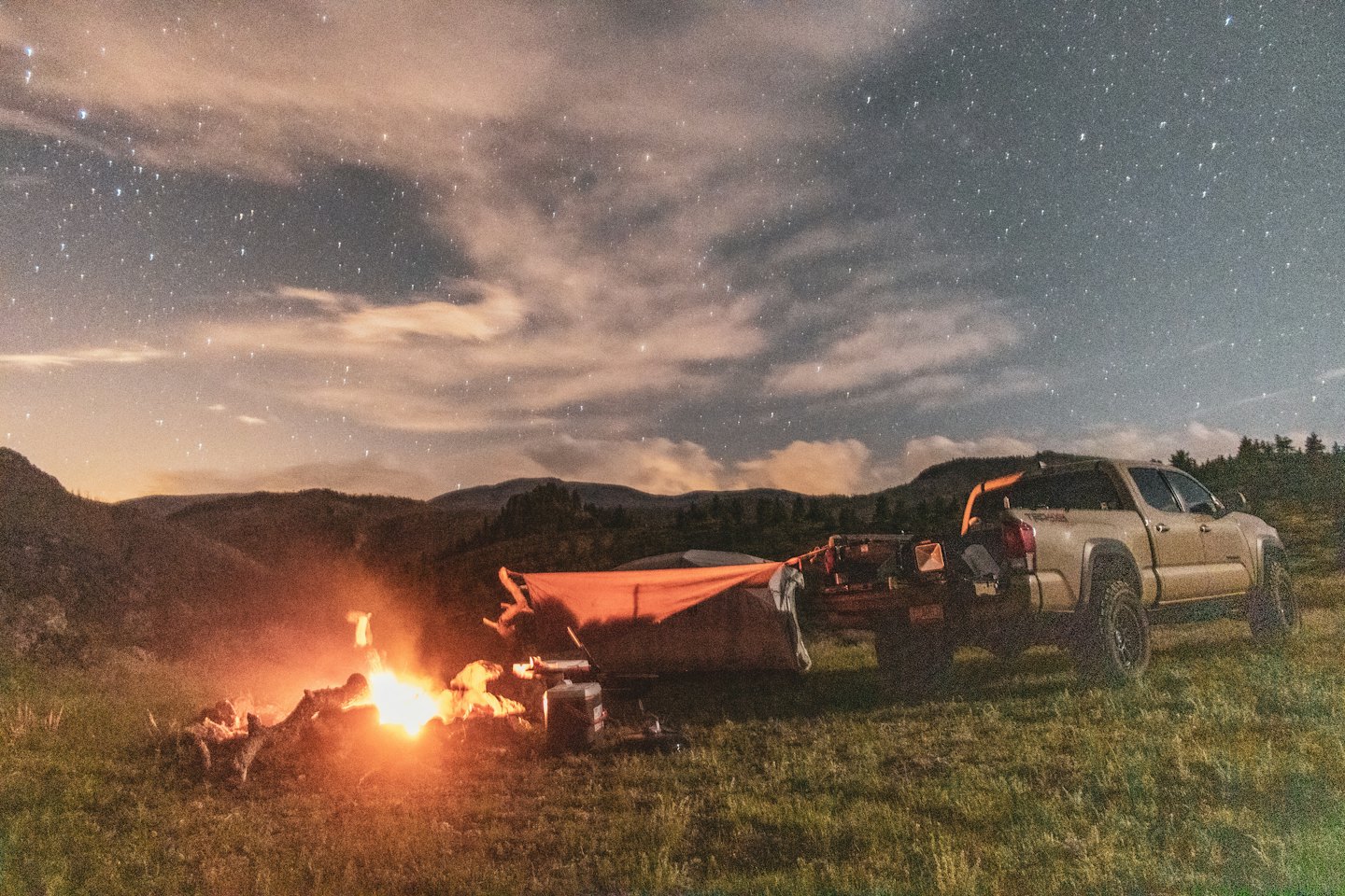 Wohnmobil und Anhänger am Lagerfeuer bei Nacht unter Sternenhimmel.