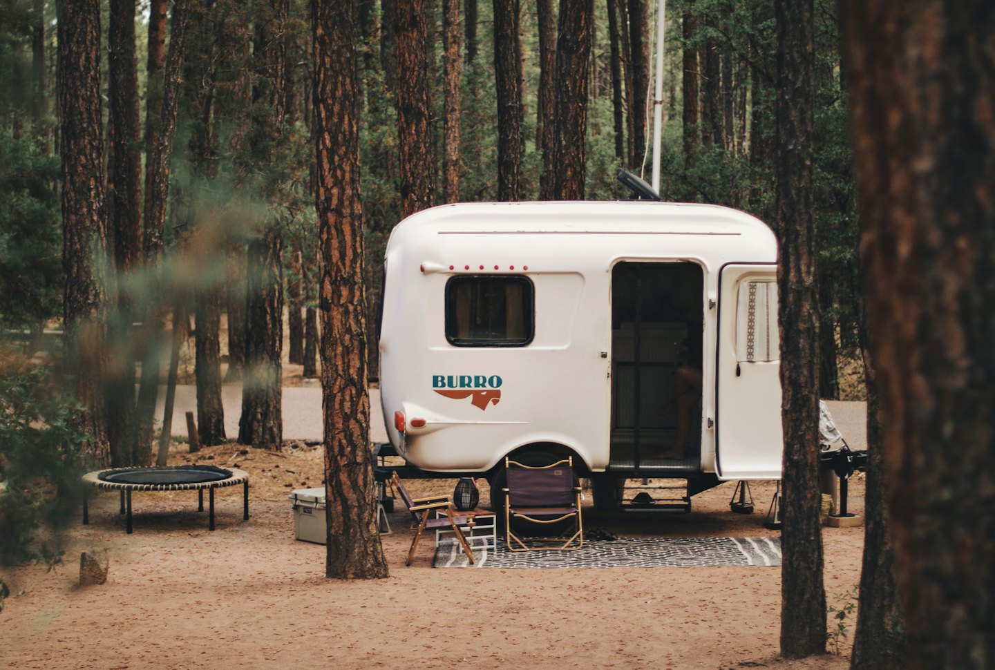 Old camper trailer with chairs in a forest.