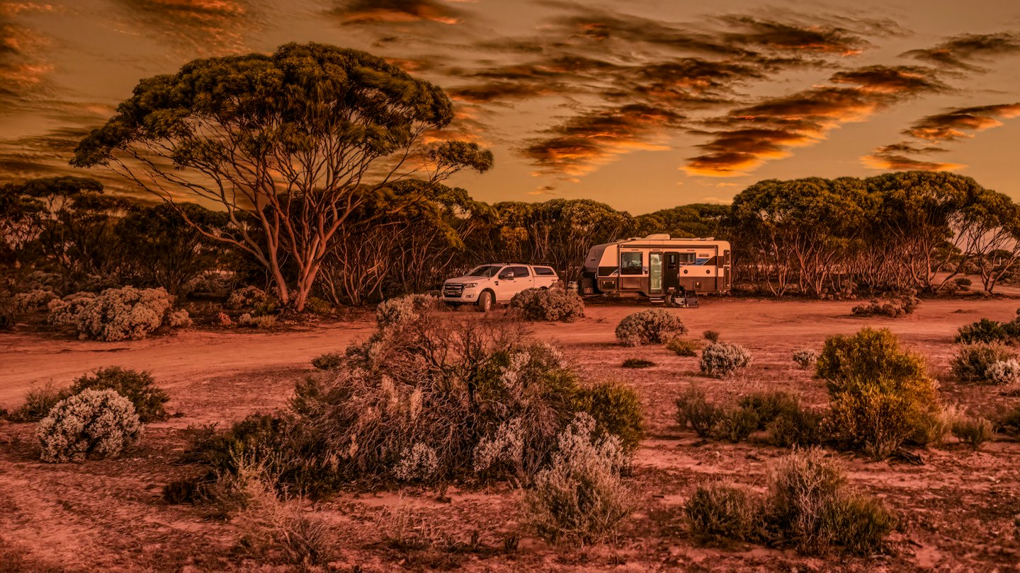 Pick-up-Truck und Wohnwagen parken bei Sonnenuntergang in trockener Landschaft.